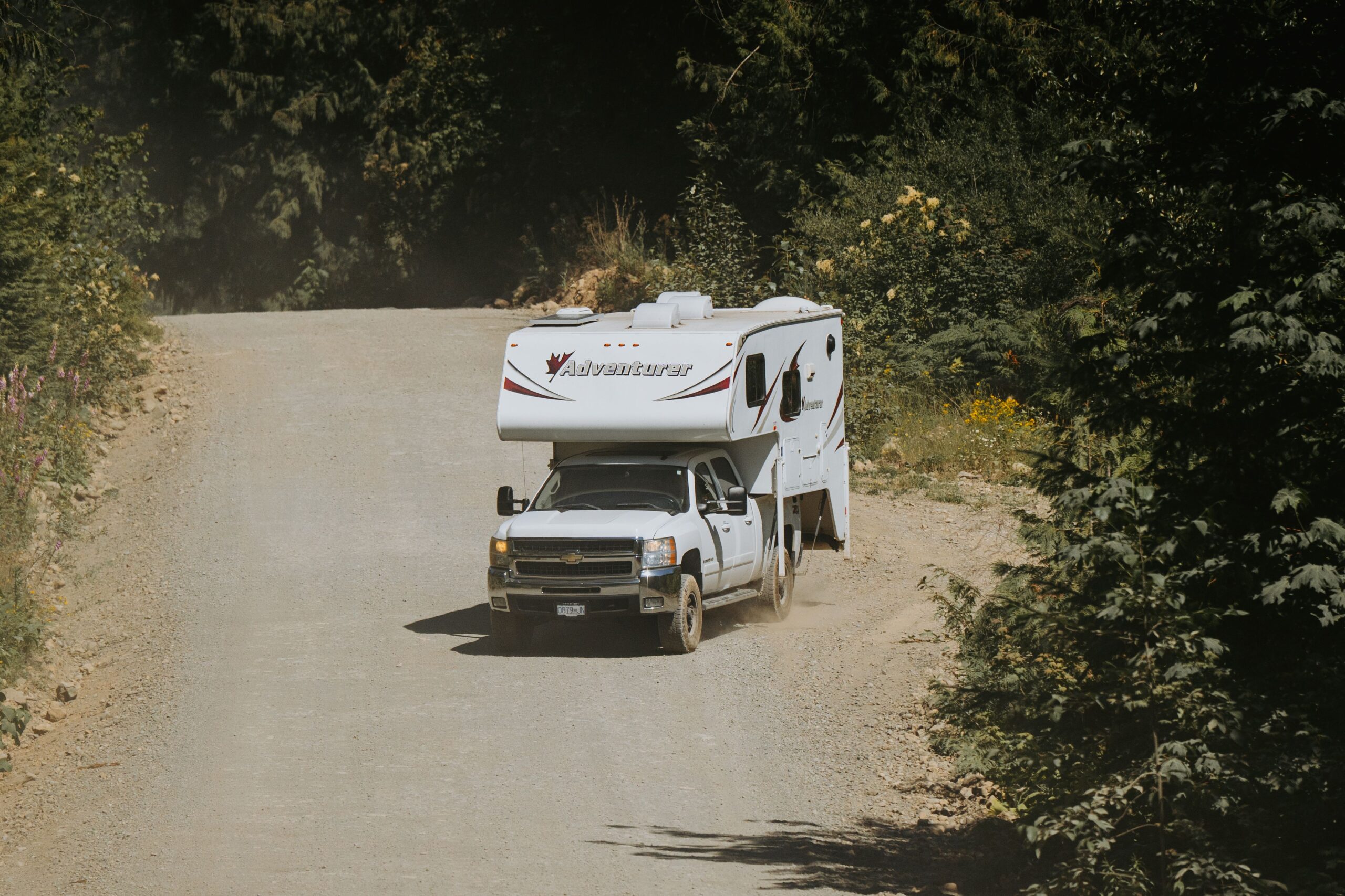Pickup truck with slide-in camper driving on a dirt road