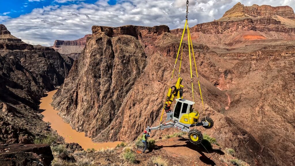 Helicopter lowers Transcanyon Waterline equipment onto a canyon ridge; Colorado River below. NPS / Sean Gunn. Public domain.